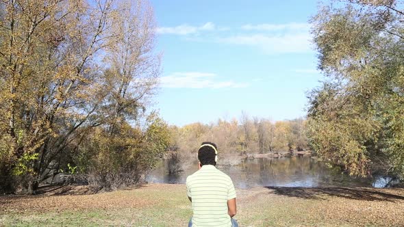 Man Listening To Music Using Headphones While Sitting By Lake 2