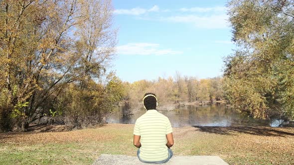 Man Listening To Music Using Headphones While Sitting By Lake 3