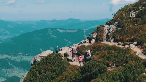 Group of Tourists and Children with Backpacks Go Down on Stone Trail in Mountain