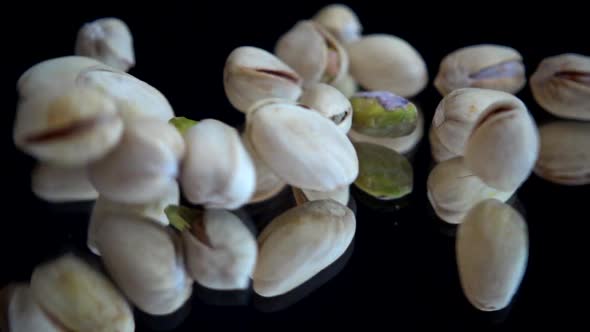 Pistachio nuts fall on a black mirror surface