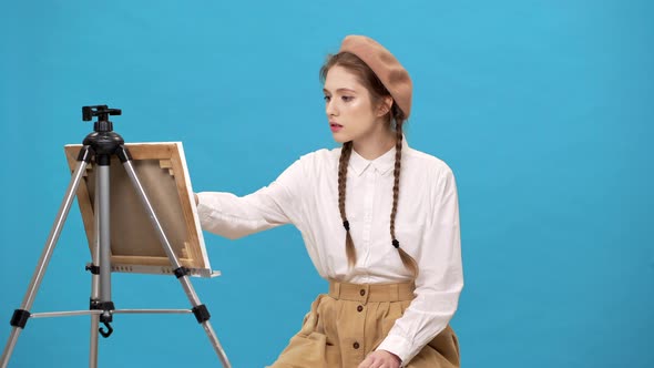 Portrait of Young Woman Artist with Two Braids Drawing on Canvas with Brush at Workshop or Master