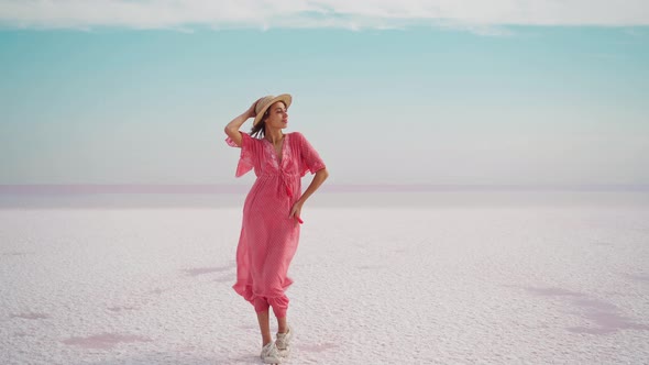 Happy Carefree Elegant Woman in Blowing Pink Dress and Straw Hat Posing on White Salty Deserted