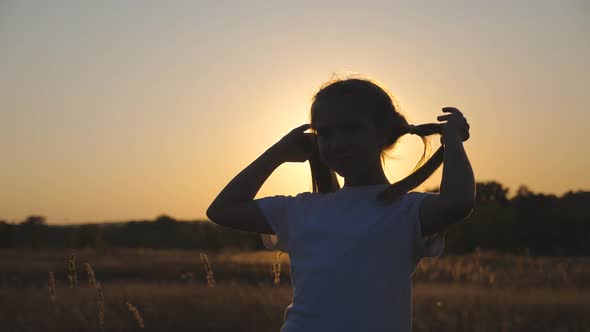 Close Up of Little Smiling Girl Look Into Camera Standing in Meadow and Playing with Her Hair