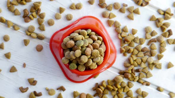 Top View of Dry Pet Food in a Red Bowl Rotating on a Wooden Table