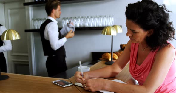 Woman writing on a diary at bar counter