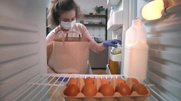 Young Woman in Safety Gloves and Mask Put Groceries in Fridge