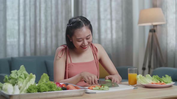 Smiling Asian Woman Slicing Cucumber While Preparing Healthy Food At Home