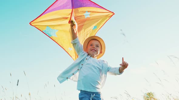 Fast Little Boy Runs Across the Field with a Kite in His Hands Fluttering in Wind Over His Head