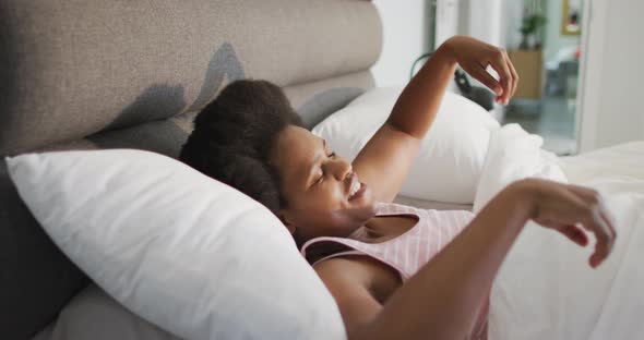 Happy african american woman lying in bed, stretching in bedroom