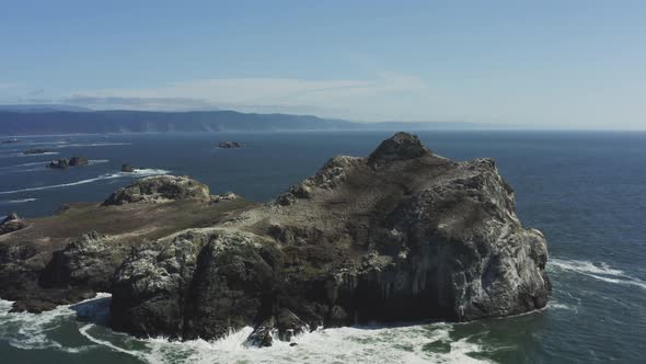 Aerial drone footage, slowly tracking around a very large Pacific ocean boulder which is surrounded