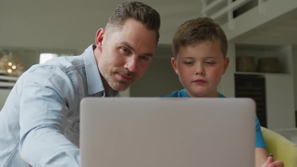 Caucasian father with son sitting at table and learning with laptop at home