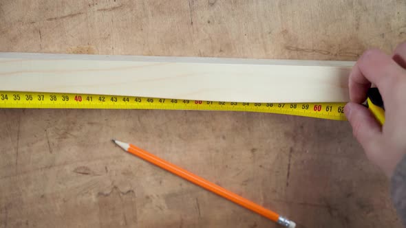 Hand Measures the Length of a Wooden Block with a Tape Measure Closeup