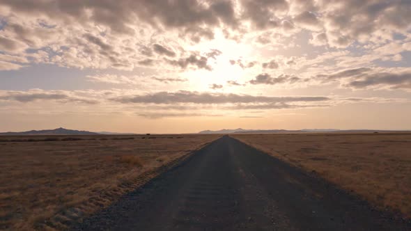 Driving on dirt road over flat vast Utah desert towards the sun