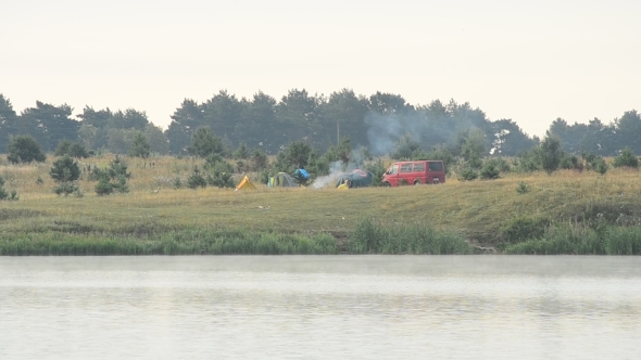 Smoke From Fire In Camp With Tents And Car On River Bank