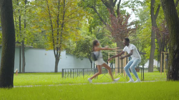 Wide Shot of Joyful African American Girl Running To Smiling Man on Sunny Day. Happy Brother Hugging