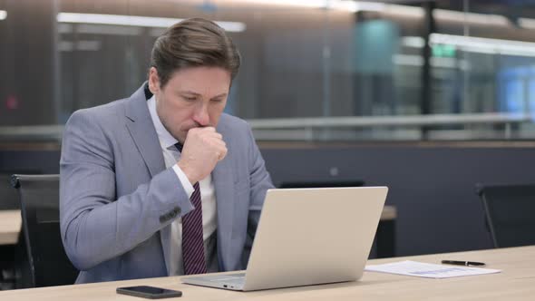 Middle Aged Businessman with Laptop Coughing in Office 