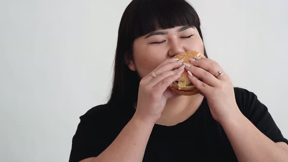 the Girl of Asian Appearance Eats a Burger and Enjoys the Taste. Not a Healthy Diet for Young People