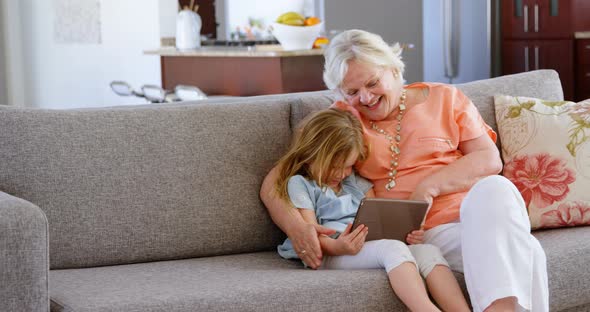 Grandmother and granddaughter using digital tablet in living room 4k
