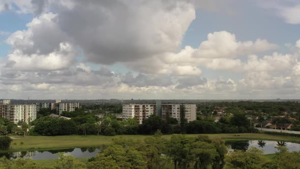 An aerial view of a reflective pond, surrounded by white apartment buildings and green grass on a su