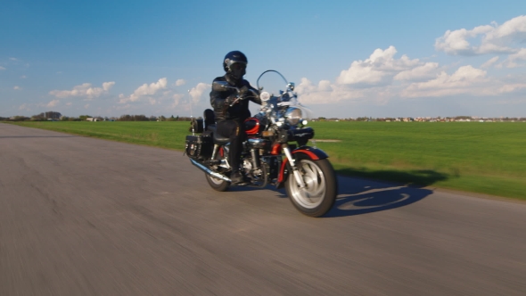Biker Rides On The Road On a Background Of Green Fields