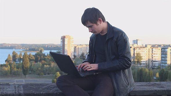 Man Sits on the Roof and Typing on Laptop