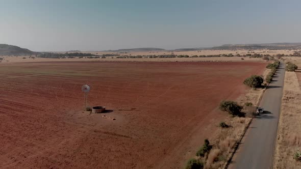 Aerial fly over of a working windpump in a dry field with a gravel road