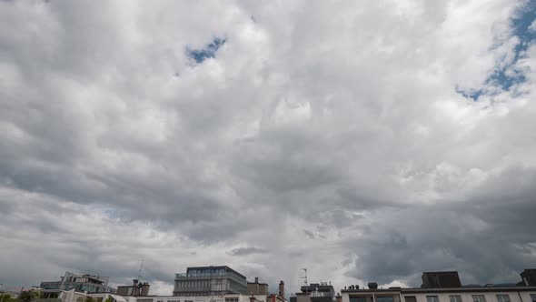Time Lapse of Fast moving white clouds over urban rooftops against a blue sky. alt