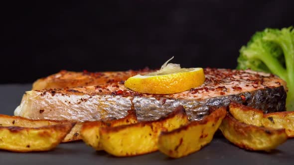 Baking salmon fillets rotating on a black background with lemon slice, french fries