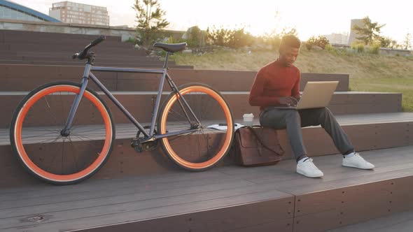 African American Man with Bike Working on Laptop in Park