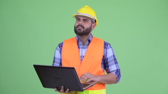 Happy Young Overweight Bearded Indian Man Construction Worker Thinking While Using Laptop