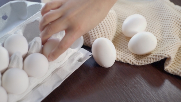 Chicken Eggs In Carton On Kitchen Table. Hand Takes Out Eggs From Carton