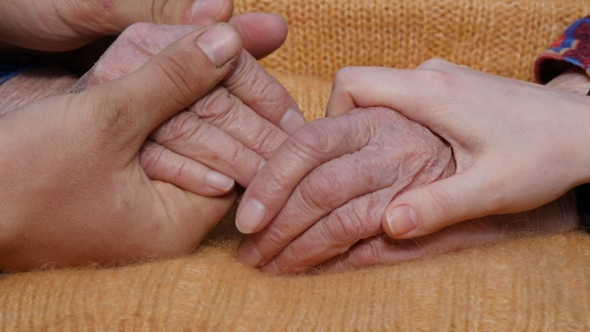 A Young Man's And Woman's Hands Comforting a Old Pair Of Hands Of Grandmother Outdoor.