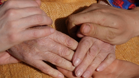 A Young Man's And Woman's Hands Comforting a Old Pair Of Hands Of Grandmother Outdoor.