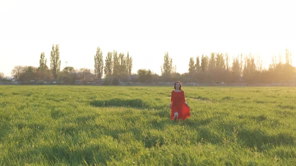 Beautiful Young Woman in a Red Dress Running in a Green Wheat Field at Sunset or Dawn