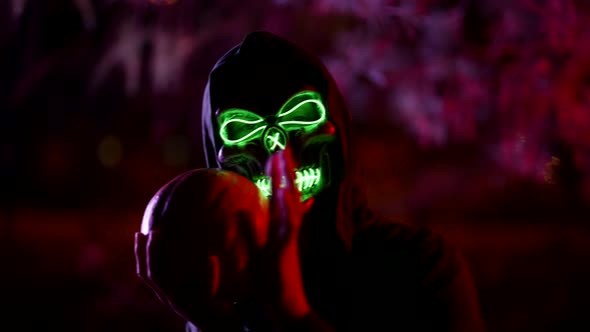 Portrait of a Person in a Mask of Death and in a Hood Against the Background of Branches Illuminated