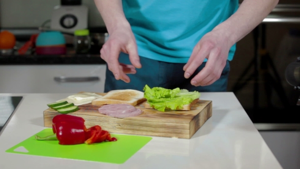 Man Making Sandwich On Cutting Board In Kitchen