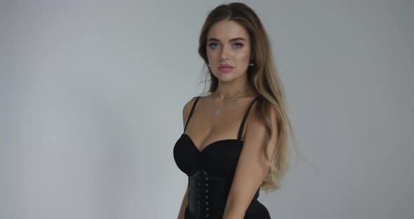 Attractive Young Girl Waving Her Hair in a Black Corset, Flirtatious Looking at the Camera