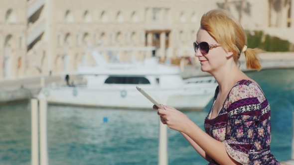 Young Woman Enjoying a Tablet Against The Background Of The Bay With Yachts