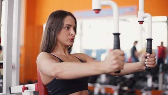 Young Woman Flexing Muscles On Cable Gym Machine.