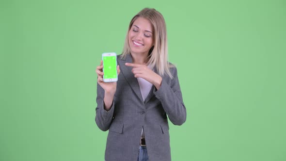 Happy Young Blonde Businesswoman Showing Phone and Giving Thumbs Up