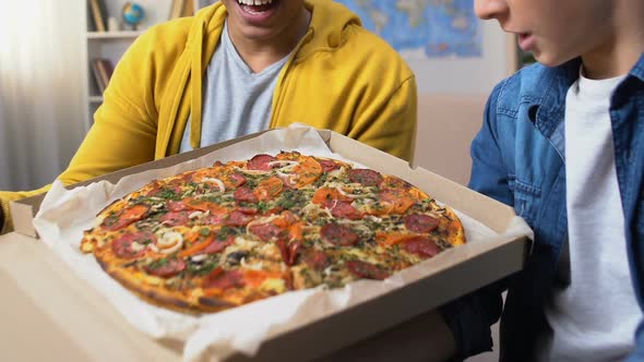 Two Male Students Opening Pizza Box and Looking at Tasty Caloried Meal, Fastfood