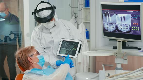 Stomatologist with Face Shield Reviewing X-ray Pointing on Tablet