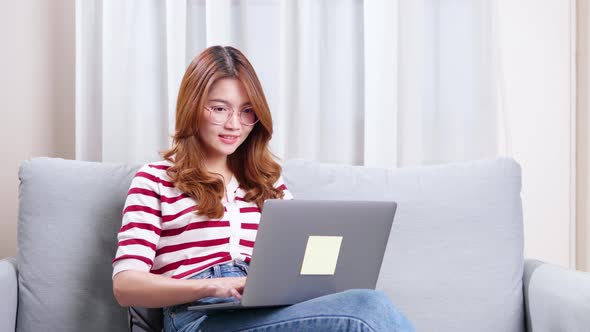 Young Asian woman sitting on sofa using notebook to shop online.