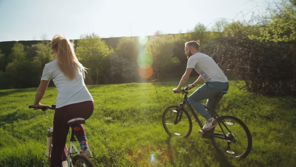 Man And Woman Riding Bicycles On The Green Meadow.