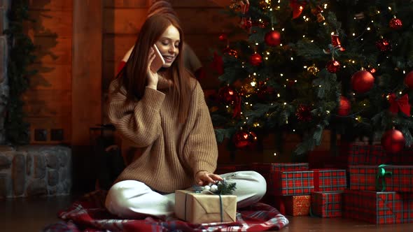 Dreamy Happy Redhead Young Woman Holding Christmas Gift in Hands and Talking By Mobile Phone.