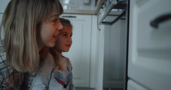 Loving Happy Mom and Daughter Watch As Cookies Are Prepared in the Oven