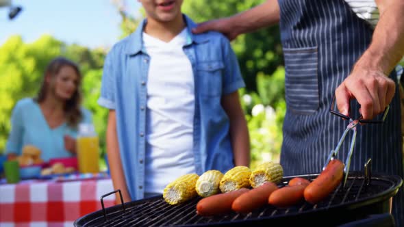 Father and son grilling sausages and corns on barbecue