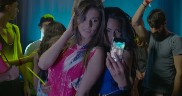 Women taking self photograph and enjoying music while dancing with friends in nightclub