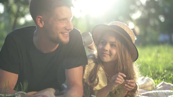 Smiling Girl and Man Talking Lying in Sunbeam on Green Spring Summer Meadow Outdoors