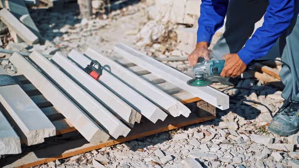 Worker is polishing stone by hand grinder outdoors. 